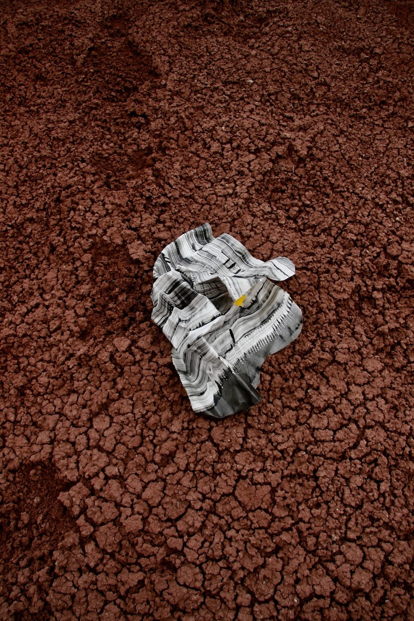 image of crumpled black and white print on a cracked red earth