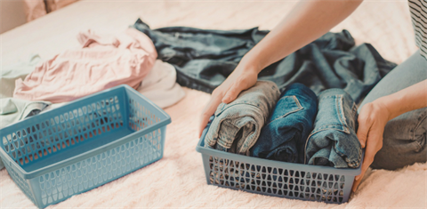 Person putting folded jeans in a basket.