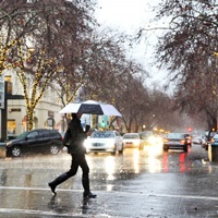 man walking across the street with umbrella over head during a rainstorm